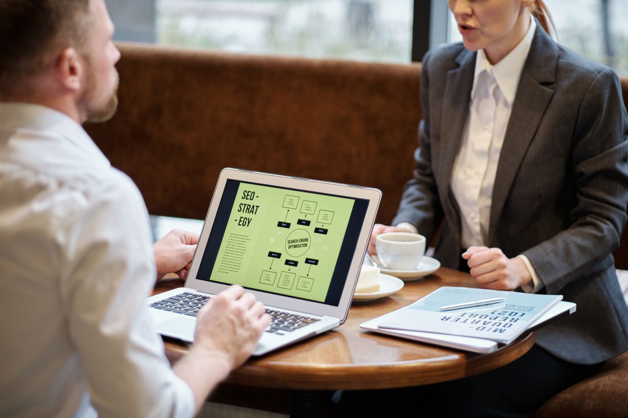 A man and woman engaged in a business meeting discussing SEO strategy in a cozy cafe setting.
